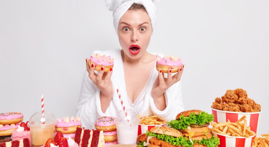 Жена стои пред маса затрупана с вредна храна.