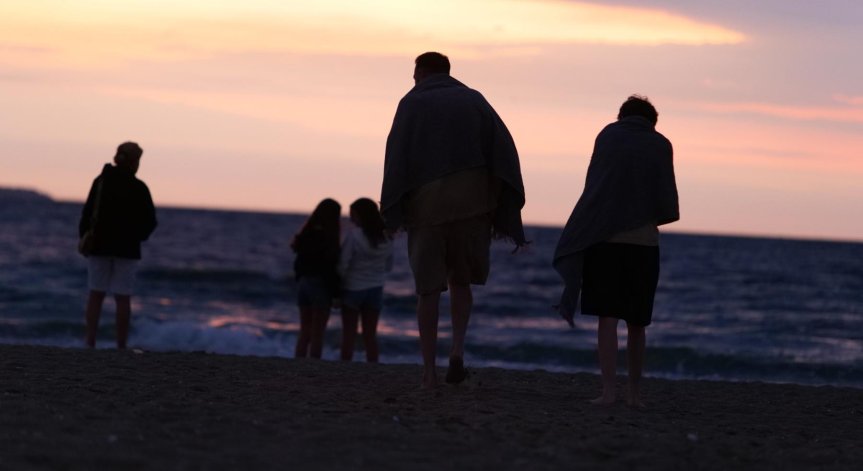 Млади и стари посрещат изгрева на слънцето на брега на морето. 